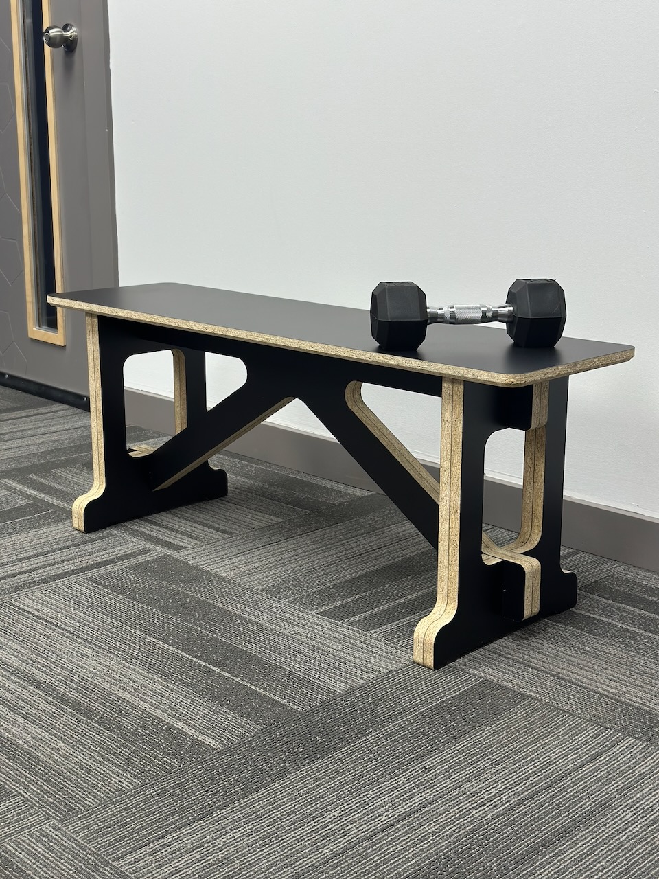 Black plywood gym bench with dumbbell on top
